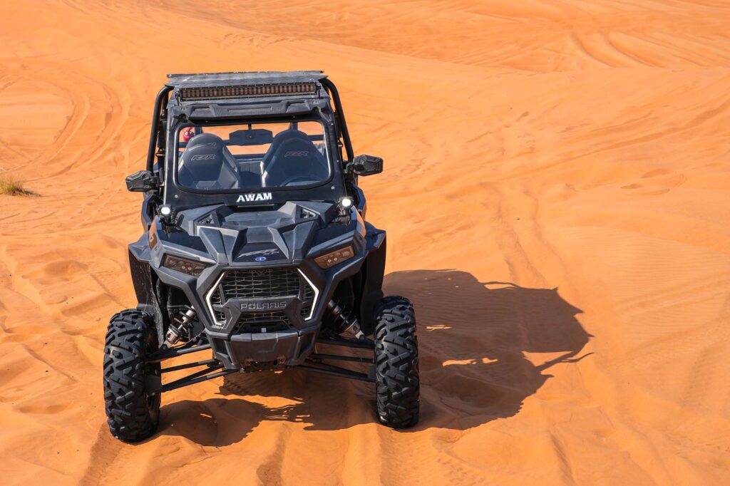 Polaris buggy climbing sand dune under clear Dubai sky